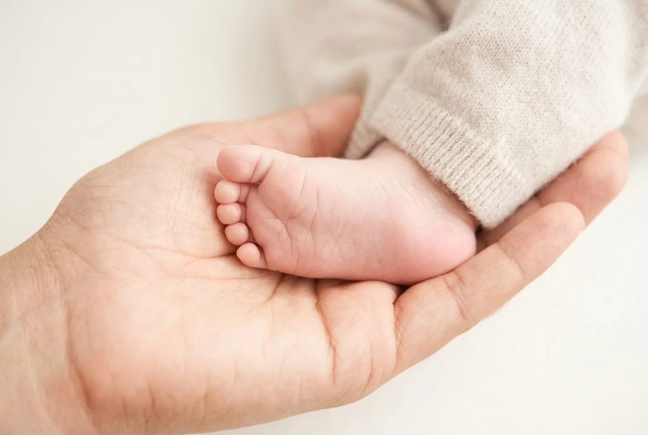 A newborn's foot resting in an adult's open palm