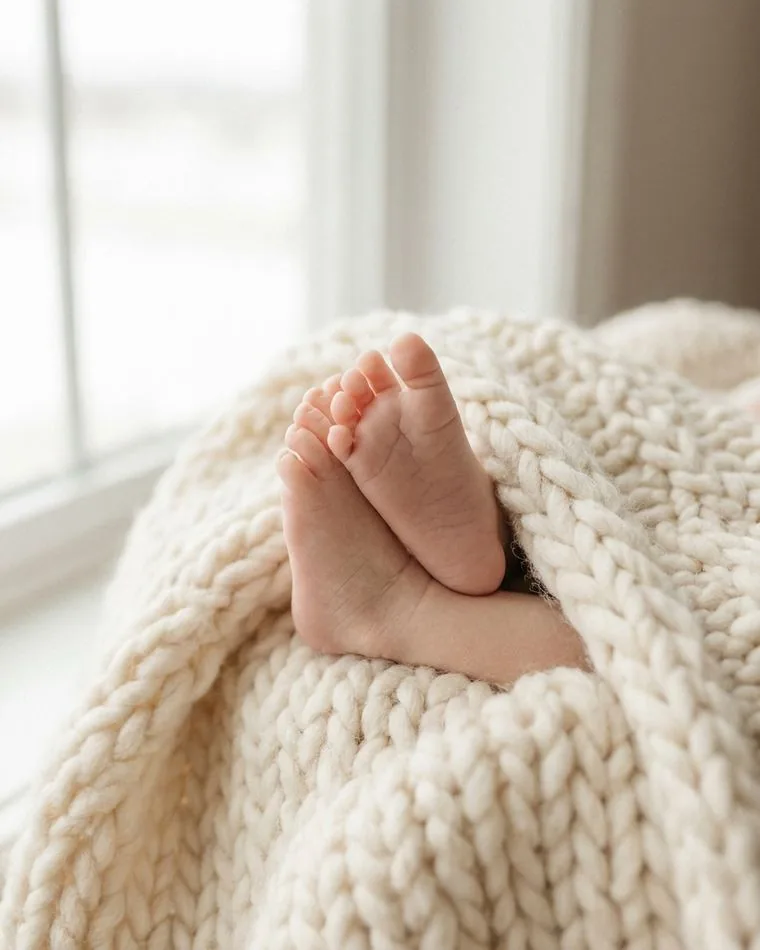 A newborn's bare feet resting in a cream knitted blanket