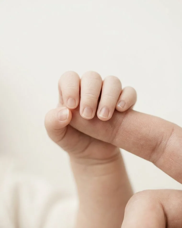 A newborn's fingers curled around an adult's fingertip