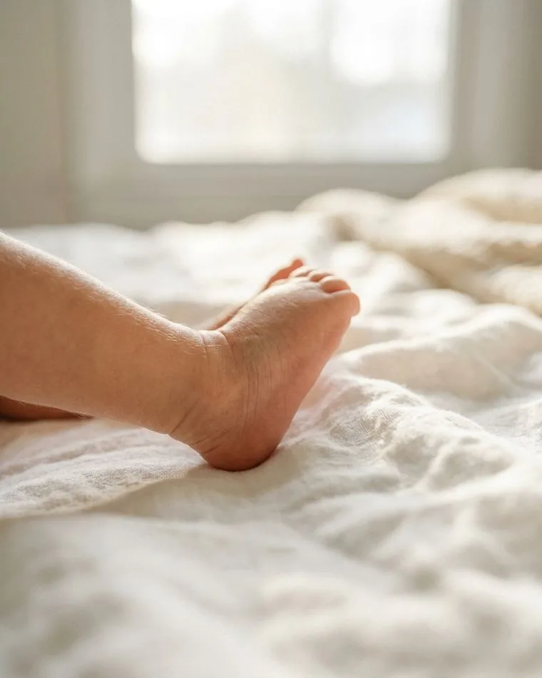 A newborn's foot resting on soft white linen in window light