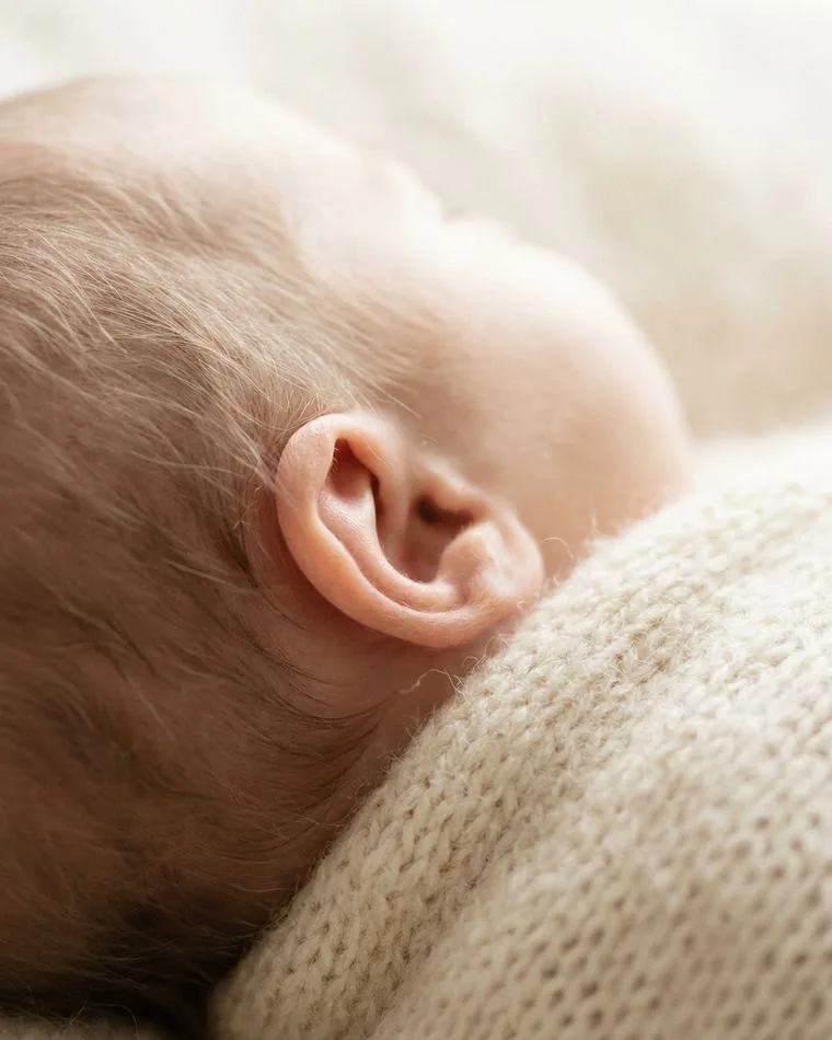 Close-up of a newborn's ear and fine hair against knitted fabric