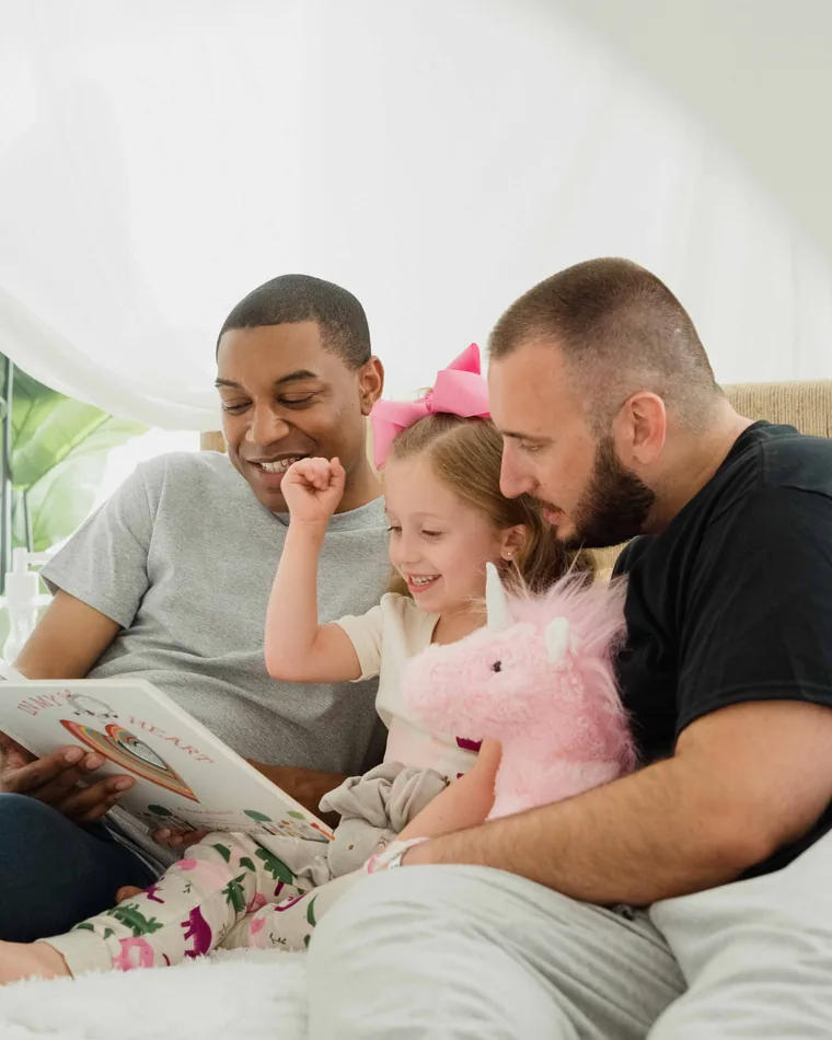 Two fathers reading a picture book with their daughter